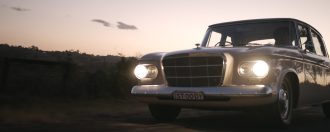 Classic car driving on country road during sunset